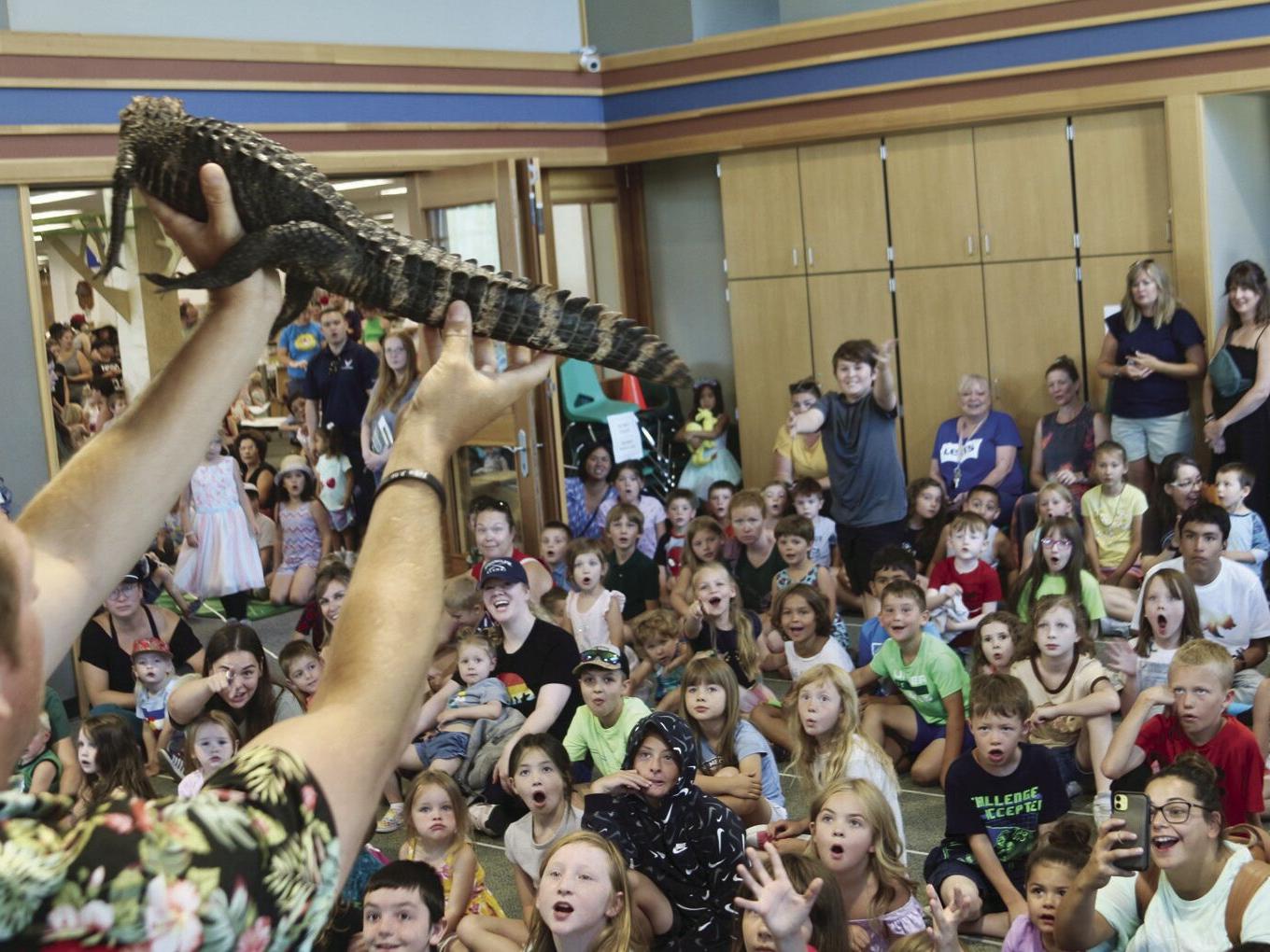A photograph of animal handler James McNamara holding a lizard up in front of a crowd of cheering children.