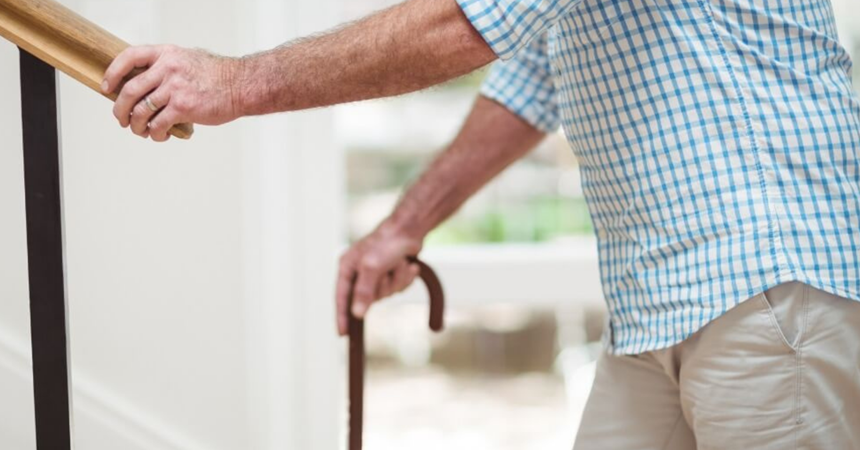 A man ascends some stairs with the aid of a cane.