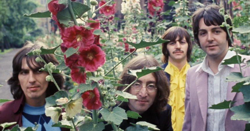 The four band members of The Beatles pose around tall hollyhock flowers.