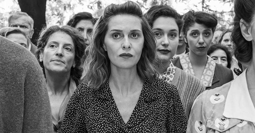 Paola Cortellesi (portraying the central character in There's Still Tomorrow) stands in a crowd with a pensive, thoughtful expression.