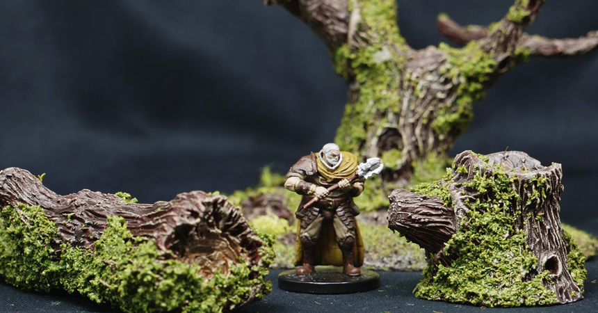 A miniature of a human fighter in heavy armor is surrounded by plastic trees covered in lichen.