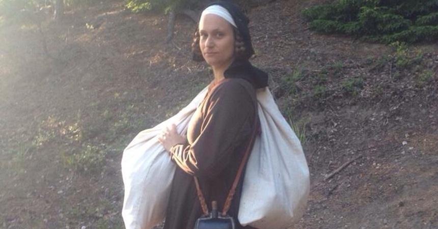 A woman in a dark brown dress carries a sack of items draped over one shoulder.