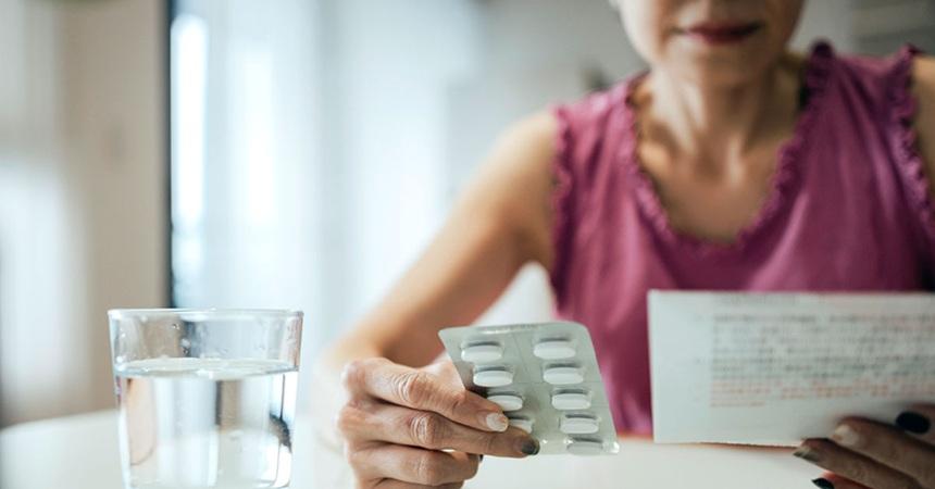 A woman looks over the information sheet for prescription medication while holding a blister pack of pills in her other hand.