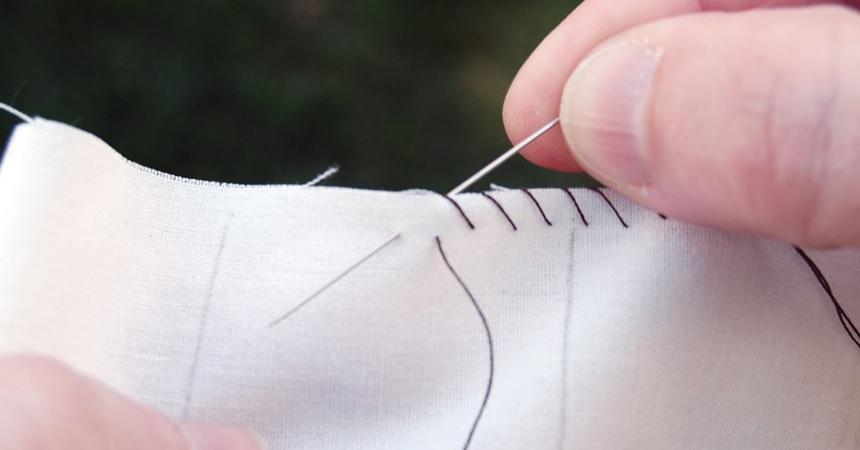 A pair of hands sews two pieces of plain muslin together.