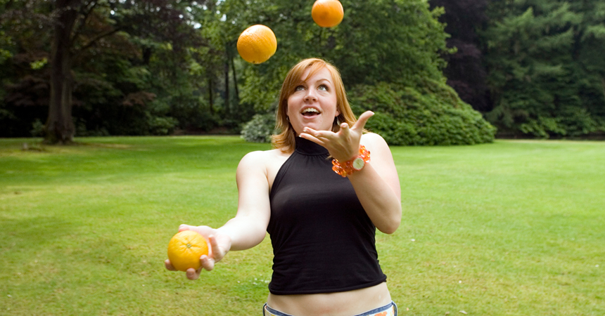 A woman attempts to juggle three oranges.