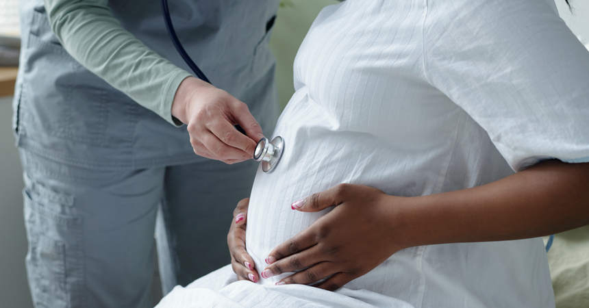 A person in hospital scrubs presses a stethoscope to a pregnant person's round belly.