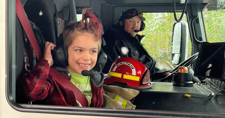 A child grins in the passenger seat of a fire engine.