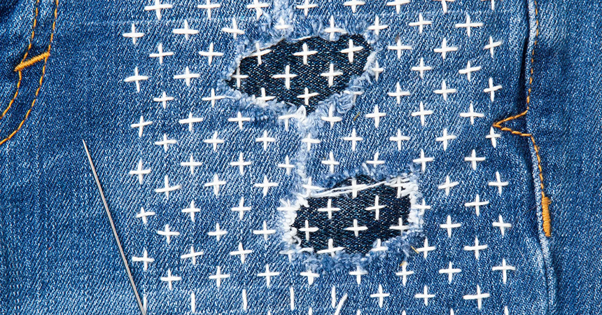 A pair of jeans mended with sashiko embroidery, a grid of cross shapes in a contrasting thread along a grid pattern.