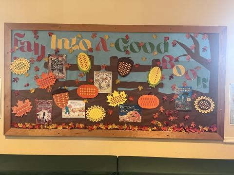 Image of Library bulletin board with autumn decorations and saying "fall into a good book"