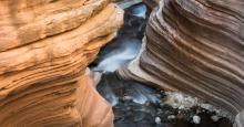A photo of a space between two rock faces at Grand Canyon National Park. Each rock face has smooth, horizontal grooves etched into them by the Colorado River.