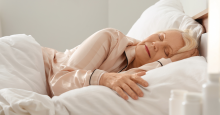 An elderly woman sleeps on her side in a fluffy, plush bed.