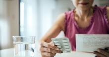 A woman looks over the information sheet for prescription medication while holding a blister pack of pills in her other hand.
