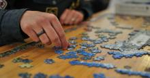 A photograph of a person solving a mostly blue jigsaw puzzle, focused on the person's hands.