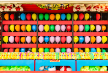 Rows of colorful balloons are set up in a dart-throwing carnival game.