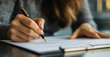 Close-up photo of a woman's hands signing a clipboard of paperwork.