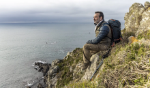 In a scene from On the Wandering Paths, travel writer Pierre Girard (played by Jean Dujardin) rests on a rocky hillside overlooking the ocean.