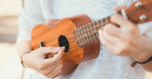 A person playing an orange ukulele.