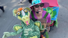 Vikki Green smiles and poses with a large green dragon puppet.