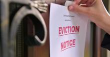 A hand tapes a sheet of paper with "EVICTION NOTICE" on it in large red letters on the front door of a home.