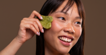 A woman presses a gua sha -- a flat, heart-shaped piece of jade -- to her cheek.