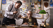 Private detective Romulo Aitken directs Sergio Chamy in how to use a magnifying glass to inspect evidence.