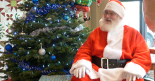 Santa Claus sits in front of a decorated Christmas tree at the downtown library.