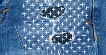 A pair of jeans mended with sashiko embroidery, a grid of cross shapes in a contrasting thread along a grid pattern.