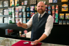 Seth Howard stands behind a counter while holding a playing card in his right hand