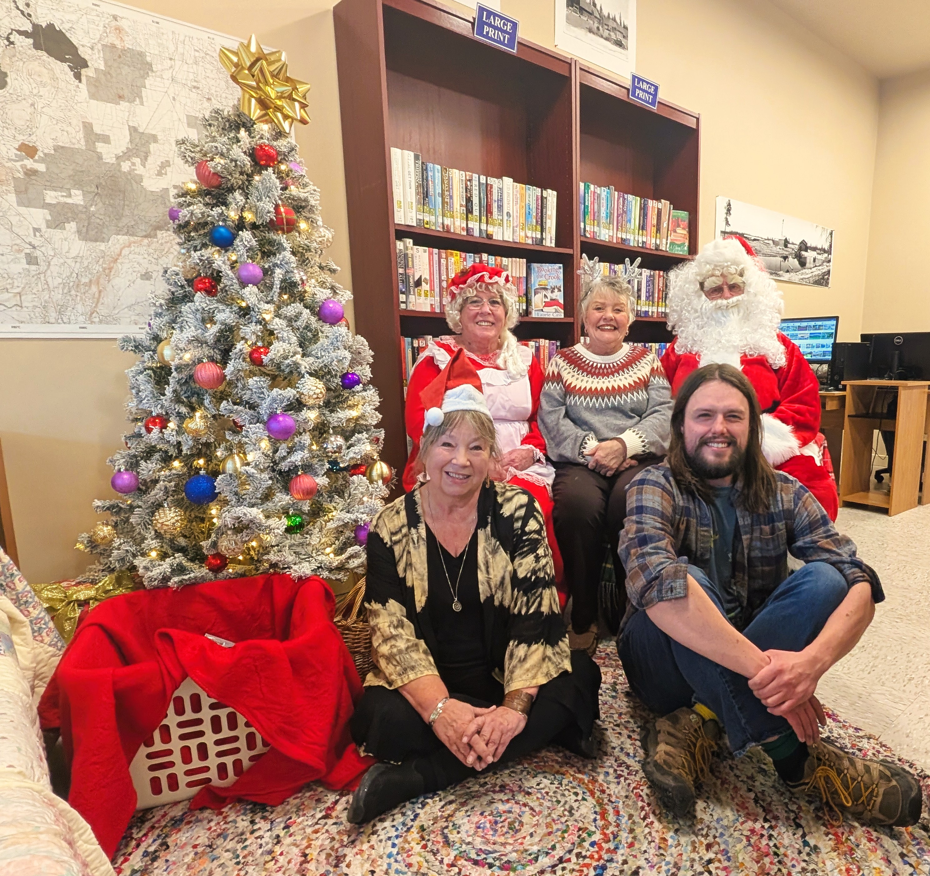 Library staff sitting by a Christmas Tree with Santa and Mrs. Claus